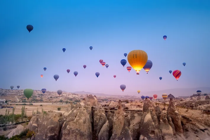 A vibrant sky filled with colorful hot air balloons floating over unique rock formations and a serene landscape at dawn.