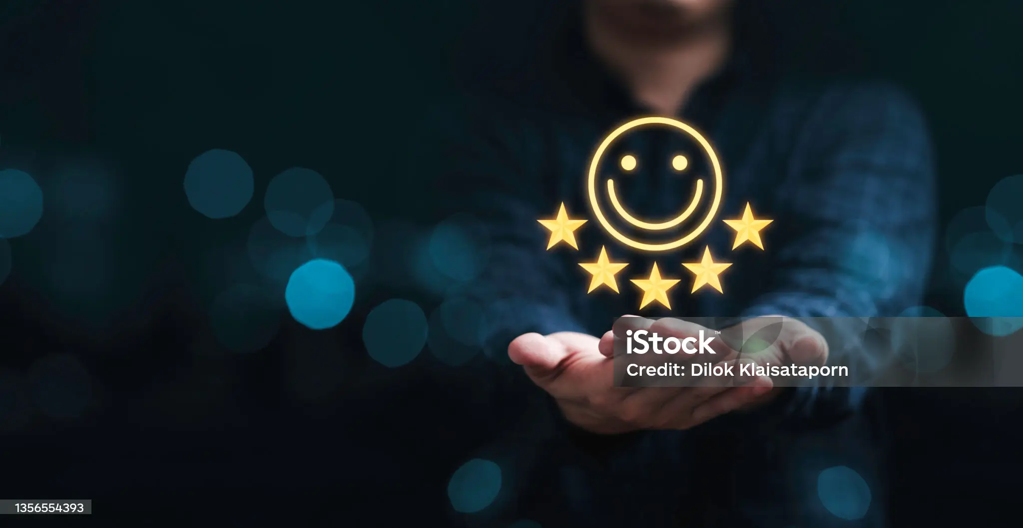 The image depicts a person holding a glowing, black smartphone in their left hand, with the screen facing outward. The phone is adorned with three gold stars and a smiley face above them. **Key Features:** * **Phone:** Black, glowing smartphone with a screen facing outward. * **Design Elements:** Three gold stars and a smiley face above them on the screen. * **Background:** Dark blue background with blurred lights or circles scattered throughout. * **Watermark:** "iStock" watermark in the center of the image, indicating that it is a stock photo. **Overall Impression:** The image appears to be a stock photo designed for use as an icon or graphic element. It conveys a sense of happiness and satisfaction, making it suitable for various digital applications where a positive emotional tone is desired.