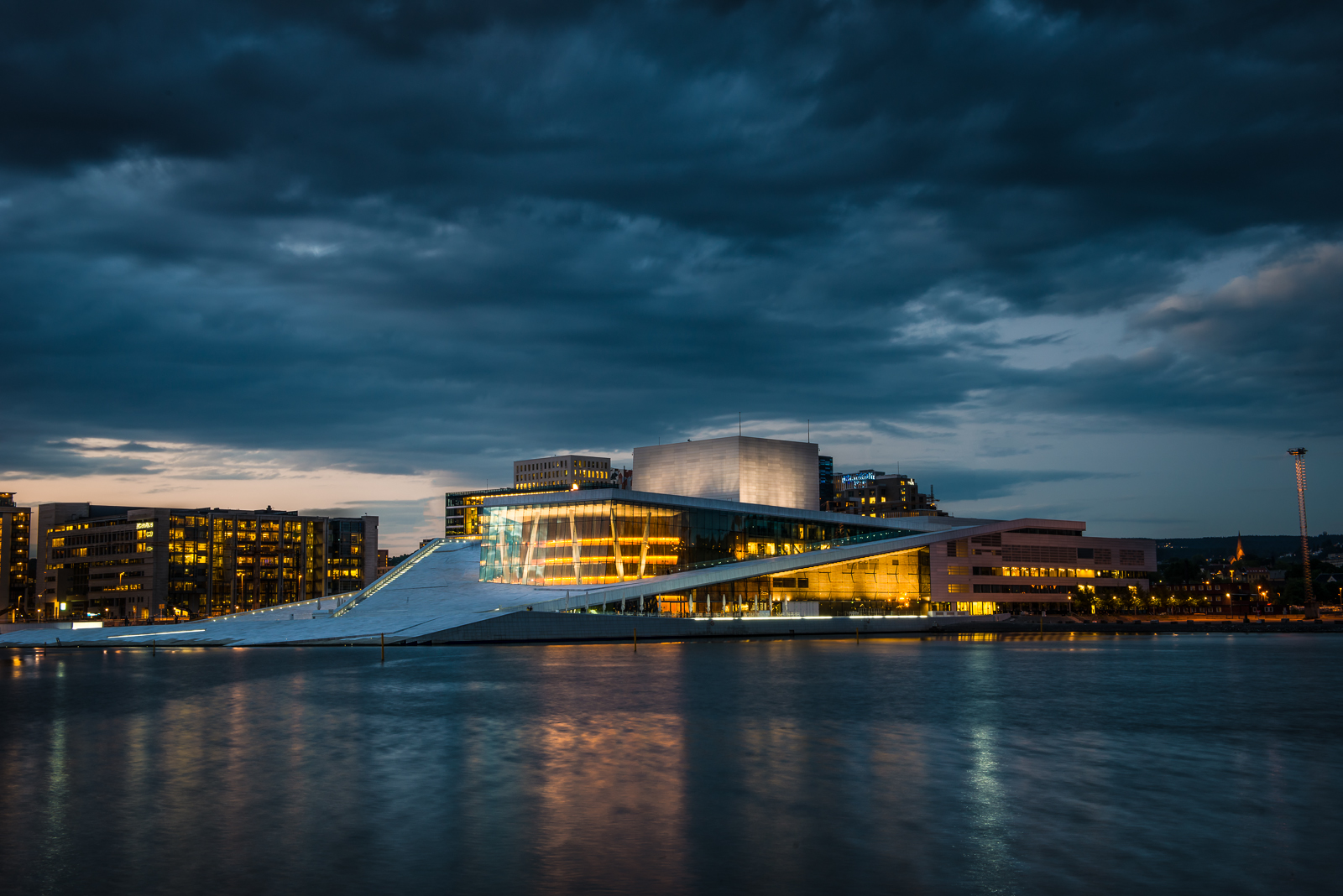 The image depicts the Oslo Opera House, a modern and sleek building situated on the waterfront of Oslo, Norway. The structure's unique design features white marble steps that lead up to the main entrance, providing an inviting path for visitors. * **Oslo Opera House** * A modern and sleek building with a unique design * White marble steps leading up to the main entrance * Situated on the waterfront of Oslo, Norway * **Waterfront Location** * The opera house is located near the water's edge * Provides stunning views of the surrounding area * A popular spot for both locals and tourists * **Unique Design** * The building's design is characterized by its use of white marble and angular lines * Creates a striking visual effect against the city skyline * Reflects the city's commitment to modernity and innovation In summary, the image showcases the Oslo Opera House as a symbol of contemporary architecture and cultural excellence. Its waterfront location offers breathtaking views, while its unique design sets it apart from other buildings in the area.