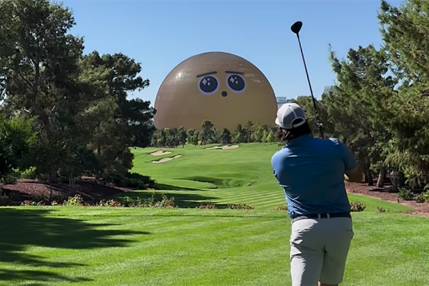 A golfer swings on a lush green course, with a large, golden sphere resembling a cartoonish face in the background under a clear blue sky.