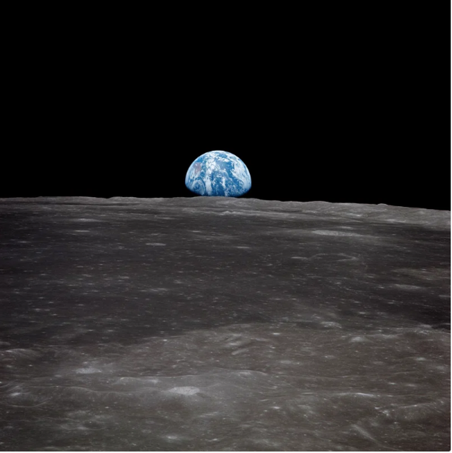 This image captures the Earth from afar, set against a stark black background. The dominant feature of the image is the Earth, depicted as a blue-and-white sphere with white clouds in the distance. A thin line of gray separates it from the blackness of space. In contrast, the foreground consists of the lunar surface, characterized by dark gray and brown hues with speckles of lighter gray. The overall composition creates a striking visual representation of our planet's place within the vast expanse of space.