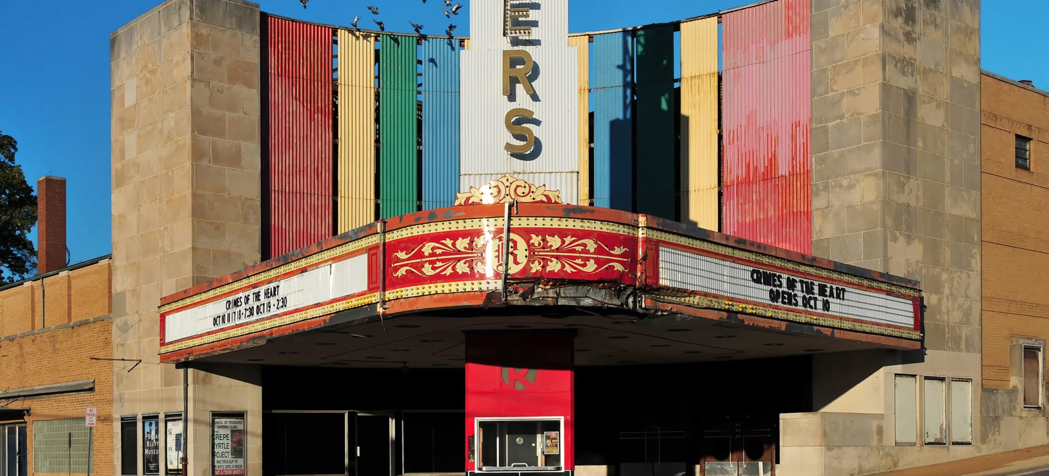 The image depicts the exterior of an old movie theater, showcasing its architectural features and signage. * The building's facade is constructed from stone or brick, giving it a classic and timeless appearance. + The stone or brick material adds texture and character to the structure. + The color of the stone or brick is a warm beige or brown, which complements the surrounding environment. * A large marquee sign with gold lettering reads "ERS" in bold letters. + The sign is prominently displayed above the entrance, drawing attention to the theater's name. + The use of gold lettering adds a touch of elegance and sophistication to the overall design. The image presents a nostalgic and charming portrayal of an old movie theater, with its unique architectural features and signage contributing to its character.