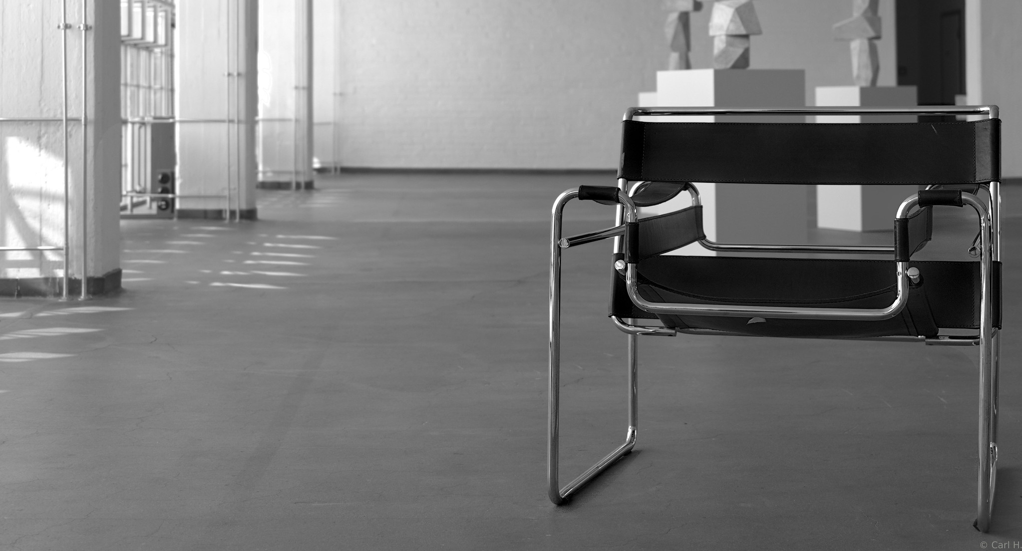 Black and chrome chair in a spacious gallery with abstract sculptures in the background, bathed in natural light.